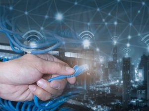 Ethernet cable held in hand by man wearing a watch against background of office buildings with WiFi connectivity